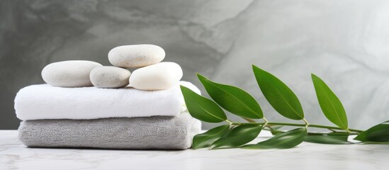 The background concept for a spa is depicted by the presence of white stones, a towel, and green plant leaves on a marble background, providing room for customization. This concept represents body