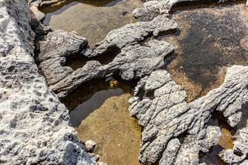 Travel close-up view, Gozo, Malta, stone wall background by the Mediterranean Sea, cliff pits and water