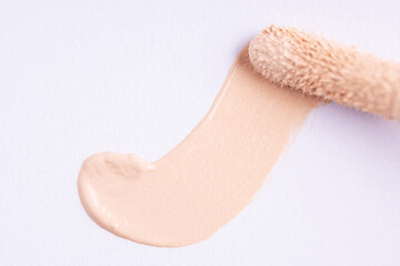 A smear of foundation cream or concealer with a applicator on a white background, macro. Texture of...