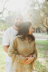 Romantic portrait of couple in the park. Man and woman with dark brown hair hugging together in the garden in nature in autumn. Olive color palette. 