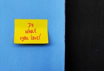Yellow note written DO WHAT YOU LOVE, on blue wall with black copy space, concept of find a job one...