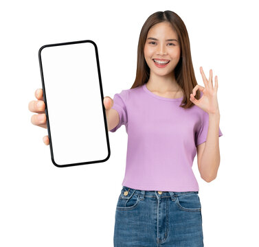 Cheerful beautiful Asian woman holding big smartphone and shows ok sign on grey background.