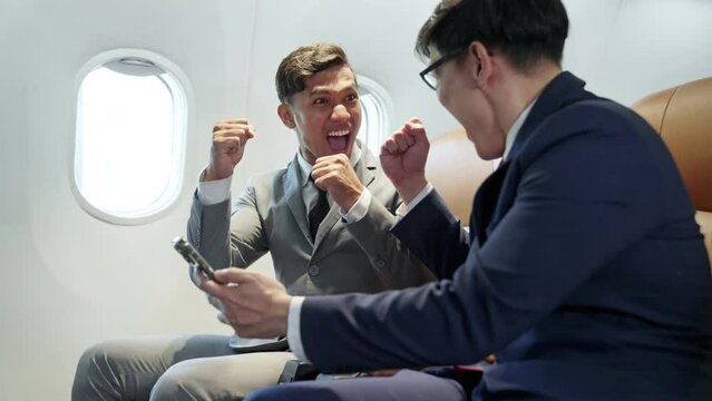Excited  young partner asian businessman sit and working on laptop in seat on the plane hand up to celebration for success of work, Play stock. Congratulation good news while flying on airplane.