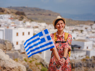 Young traveling woman with national greek flag enjoying view of Lindos. Travel to Greece,...