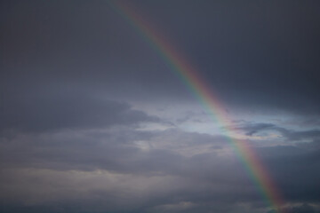 Rainbow on stormy dark sky background.