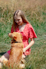 A young girl with long fair hair in a red jumpsuit hugs, strokes and plays with her dog.
- 632084058