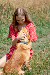 A young girl with long fair hair in a red jumpsuit hugs, strokes and plays with her dog.
- 632085090