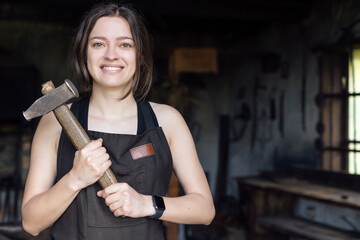 Young woman blacksmith portrait with hammer in workshop