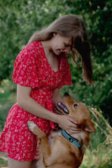 A young girl with long fair hair in a red jumpsuit hugs, strokes and plays with her dog.
- 632086201