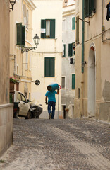 Back of a man at work in a typical Italian narrow road, in Sardinia, carrying a gas bottle