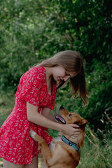 A young girl with long fair hair in a red jumpsuit hugs, strokes and plays with her dog.
- 632088479