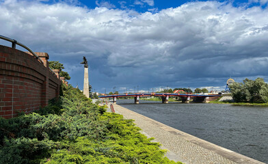 Poland, Gorzow Wielkopolski: View of the Warta River, the bridge. Varta waterfront. Sky with clouds. - obrazy, fototapety, plakaty