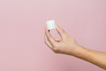 Woman's hand holding white jar (tube) with cream (ointment). Facial care, bottle with cosmetic...
