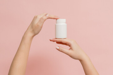Plastic bottle (tube) in hands on pink background. Packaging for vitamins, tablets or capsule, or supplement