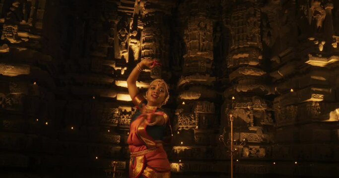 Young Indian Woman Dressed in Traditional Colorful Sari Gracefully Performs Bharatanatyam Dance in a Temple. The Low Angle Shot Captures Her Captivating Dance Moves as She Gazes at the Camera