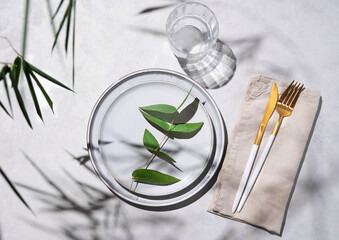 Festive table setting with white plates and glass for a spring celebration, wedding, birthday or mother's day with plant branches on a light background with morning shadow. Restaurant menu concept.