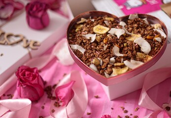 granola flavored with nuts, chocolate and banana on a pink table in a heart shaped box