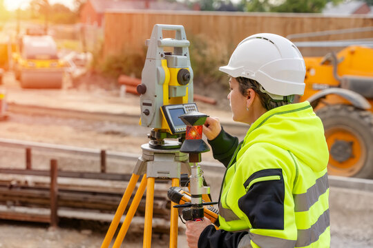 Close-up portrait of a woman site engineer surveyor working with theodolite total station EDM equipment on a building construction site outdoors