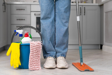 Close-up of women's legs next to a bucket of detergents and rags and a mop while cleaning the house. Concept of cleaning, household chores