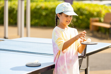 Little girl playing ping pong in park.