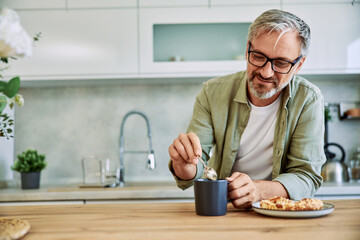 A smiling senior man drinking warm tea with a tasty breakfast at home.