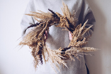 Stylish autumn wreath. Hands holding dry grass, wildflowers and wheat rustic wreath