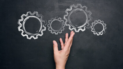 Chalk-drawn gears and a female hand on a black chalkboard, concept of teamwork
