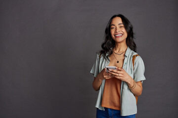 Obraz premium Multiethnic young woman using smartphone on grey wall