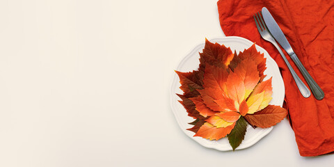 Autumn table setting, above view plate decorated red leaves and cutlery on red napkin on beige background, banner. Aesthetic autumn home and table decor. Fall holiday natural decor.