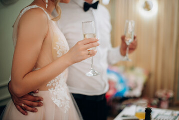 Bride and groom holding beautifully decorated wedding glasses with champagne. Wine glasses in hands on the background of wedding decorations