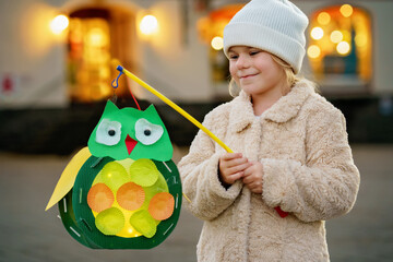 Little preschool kid girl holding selfmade traditional owl lanterns with candle for St. Martin...