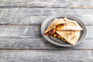 tortillas with beans on gray plate on a gray wooden background. Side view, copy space.