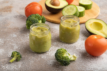 Baby puree with vegetable mix, broccoli, avocado in glass jar on brown concrete, side view