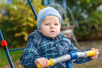 Cute little boy playing with tricycle bike outdoors. Happy child play in autumn park. Toddler baby boy wears trendy jacket. smiling Blonde boy portrait. Autumn fashion. Stylish child outside.