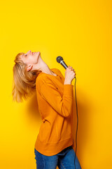 Woman having fun singing karaoke on yellow background