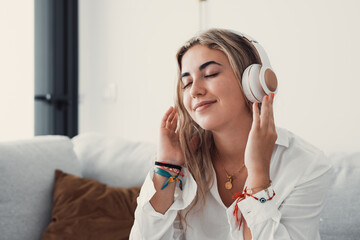 Peaceful girl in modern wireless headphones sit relax on comfortable couch listening to music, happy calm young woman in earphones rest on cozy sofa, enjoy good quality sound, stress free concept.