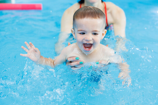 A 2-year-old boy learns to swim in a pool with a coach. Swimming lessons for children. Swimming school for children. Educational swimming courses for children