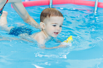Fototapeta na wymiar A 2-year-old little boy is learning to swim in the pool. Swimming lessons for young children. Swimming school for children.