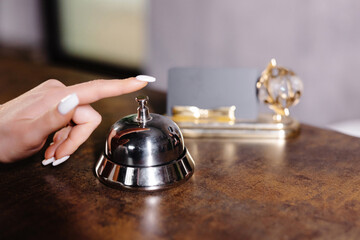 Hand of guest ringing bell on reception desk of in hotel.