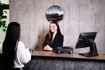 Friendly young concierge standing behind a reception counter talking room information to guest...