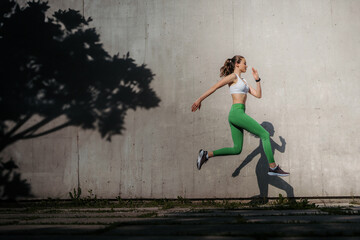 Fitness woman running in front of concrete wall casting shadow.