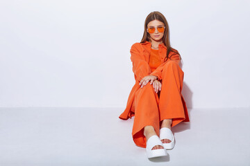 Young fashion woman in orange pants orange top orange shirt on white background. Platform slides sandals, orange sunglasses. - 632124639