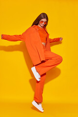 Young fashion woman in orange pants orange top orange shirt on yellow background. Platform slides sandals, orange sunglasses. - 632124658