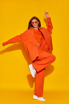 Young fashion woman in orange pants orange top orange shirt on yellow background. Platform slides sandals, orange sunglasses.