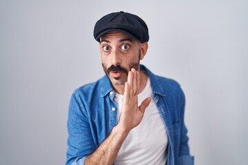 Hispanic man with beard standing over isolated background hand on mouth telling secret rumor, whispering malicious talk conversation