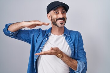 Hispanic man with beard standing over isolated background gesturing with hands showing big and...