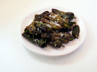 Grilled padron peppers with salt and pepper on white plate