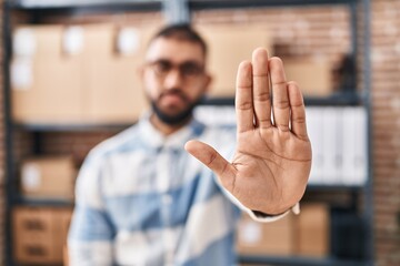 Young hispanic man ecommerce business worker doing stop gesture with hand at office