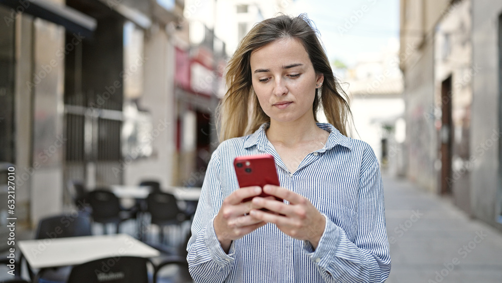 Poster Young blonde woman using smartphone with serious expression at coffee shop terrace