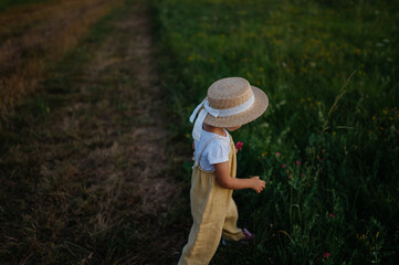 Rear view of adorable little girl with straw hat on walk during warm summer evening.